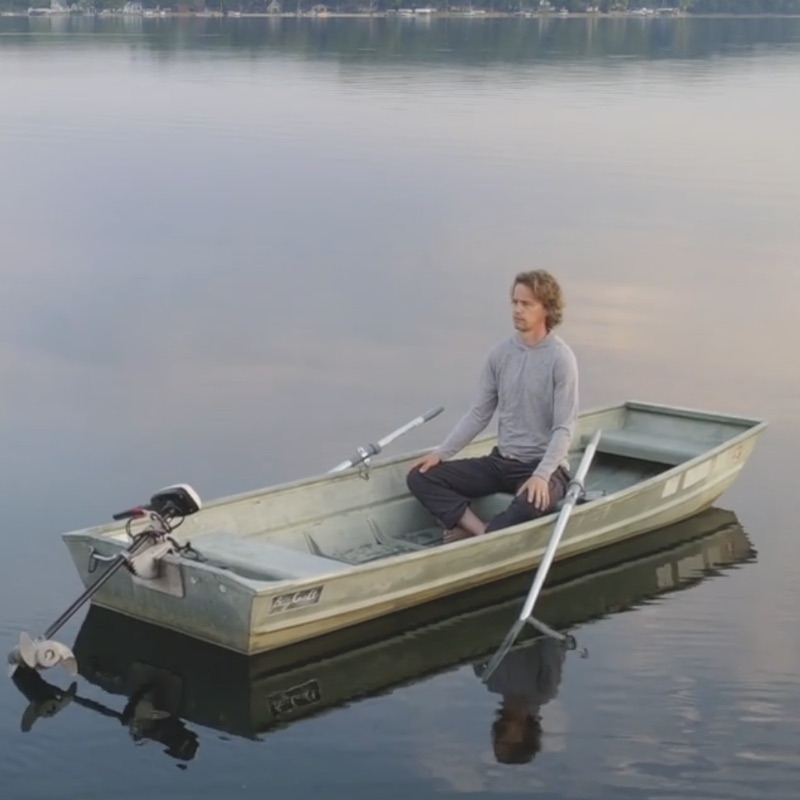 Nate sitting in a small rowboat on a still lake, reflected in the water